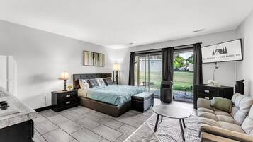 A modern bedroom with a bed, bedside tables, a nightstand, a sofa, a coffee table, and a view of the outdoors.