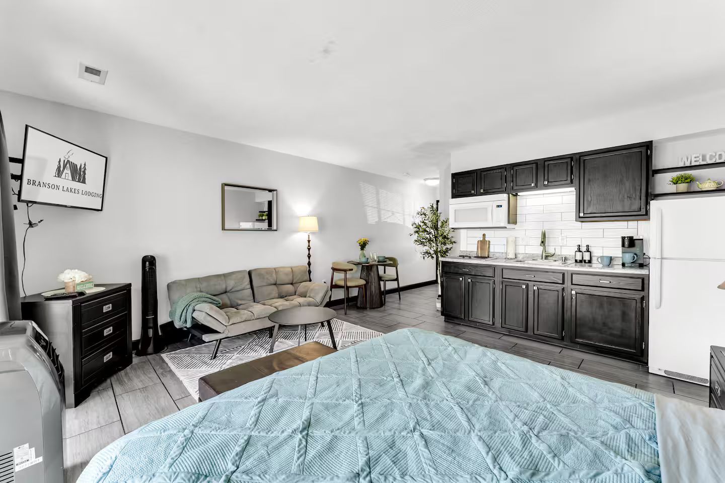 A compact living space with a kitchenette, a sofa, a dining table, and a bed with a blue quilt.