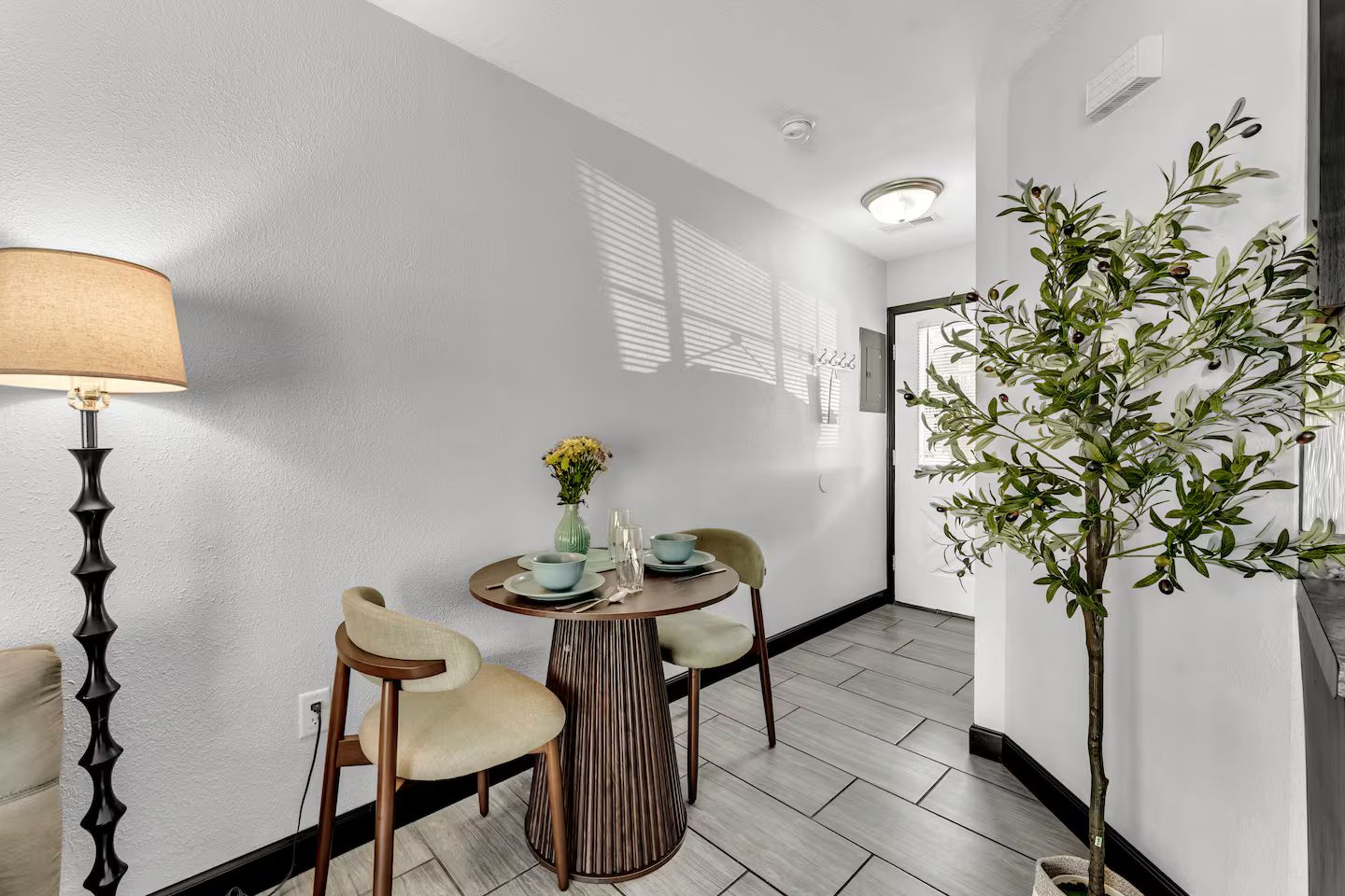 Een eethoek met een ronde tafel, twee stoelen, een vaas met bloemen en een lamp.
