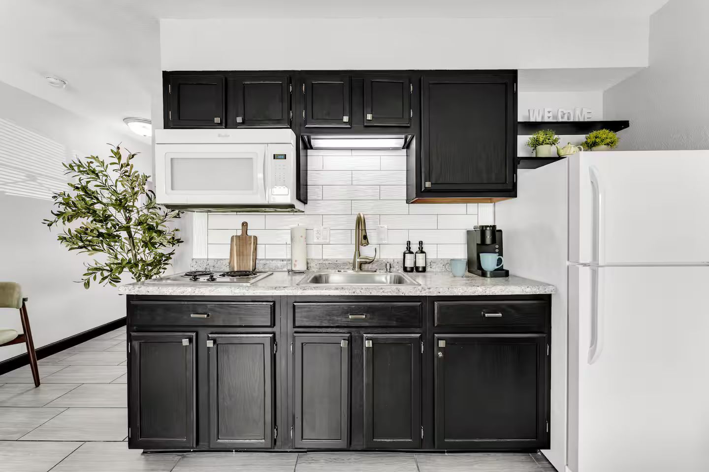 A modern kitchen with dark cabinetry, a white refrigerator, a built-in microwave, and a coffee maker.