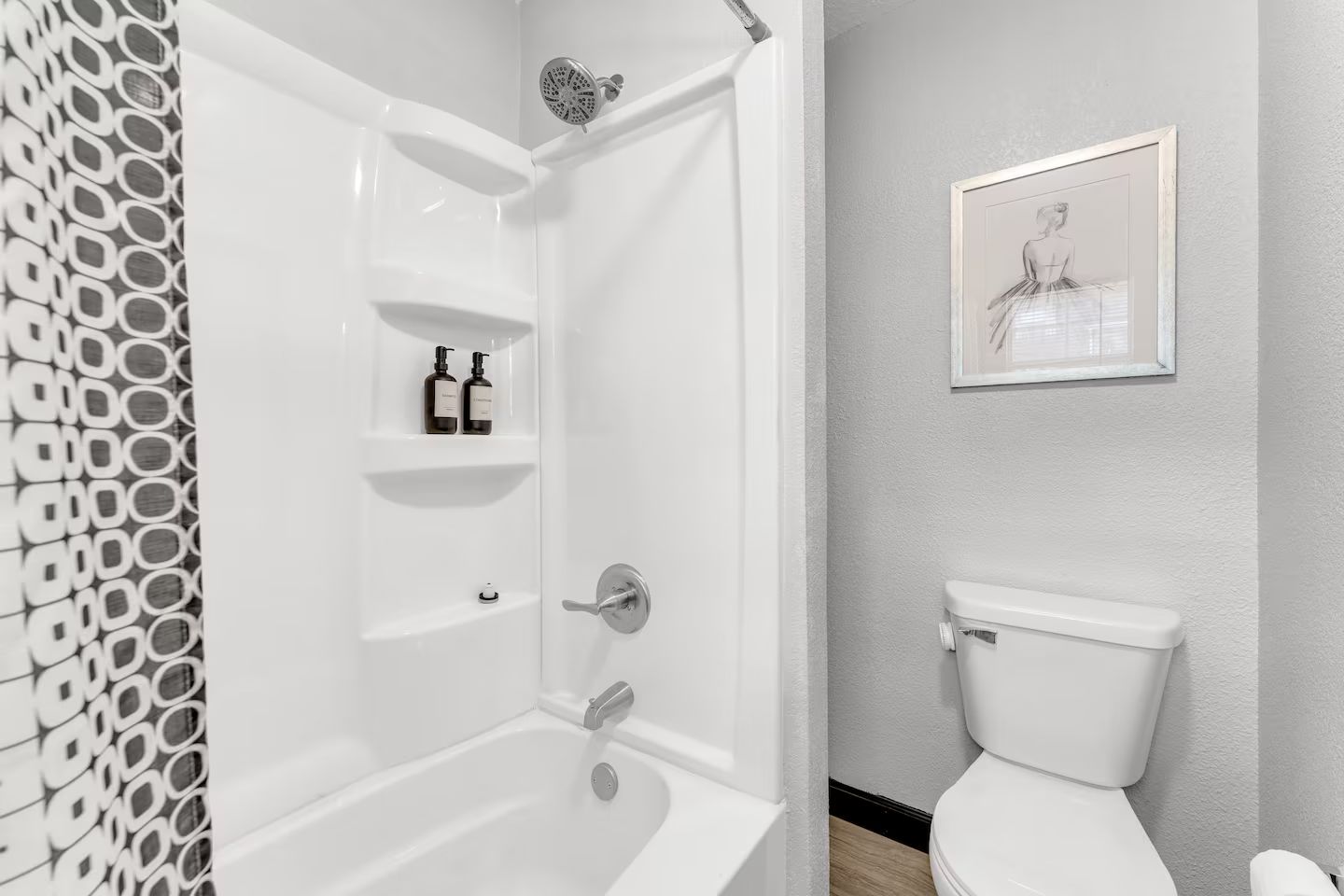 Une salle de bain avec une baignoire, des toilettes et une douche. Il y a deux bouteilles sur l’étagère au-dessus de la baignoire.
