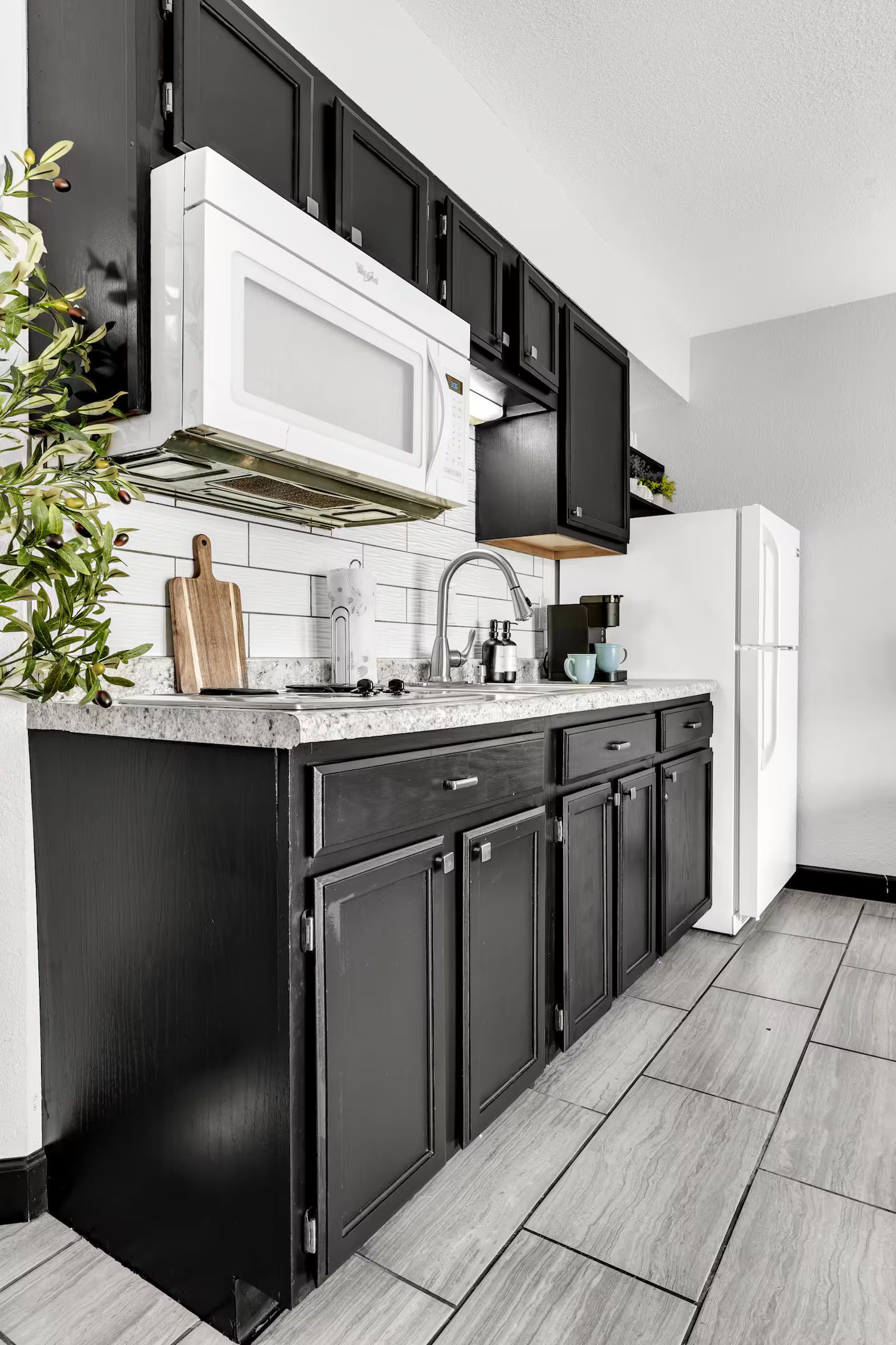 A modern kitchen with a white microwave, black cabinets, a stainless steel sink, and a coffee maker.