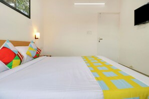 A hotel room with a bed, pillows, a nightstand, a wall-mounted TV, and a door. - Hotel O Leva Homes Near  (Bangalore)
