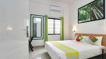 A hotel room with a bed, a window with blinds, a painting on the wall, and an air conditioning unit.