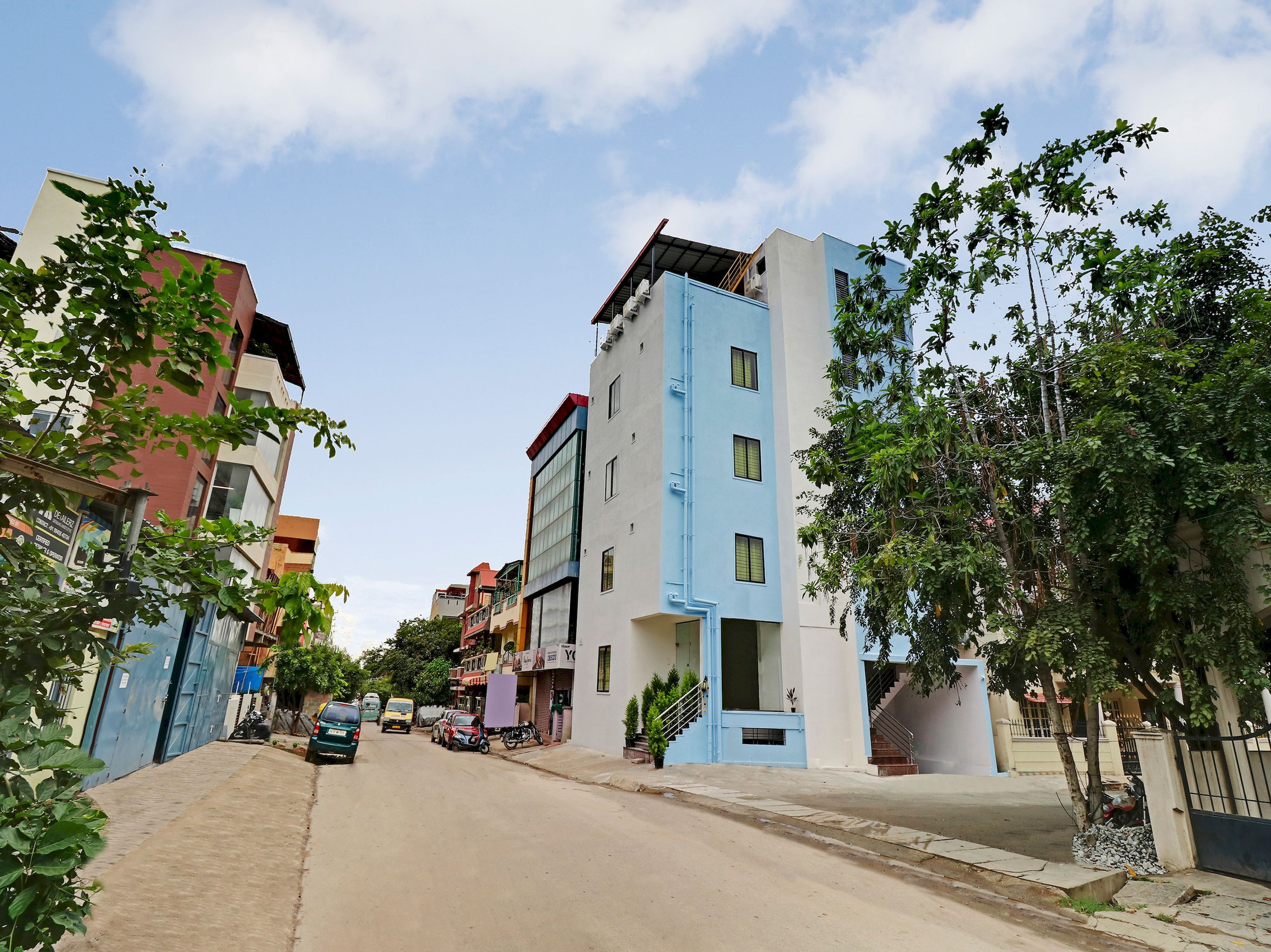 A residential street with multi-story buildings, a clear sky, and a few parked vehicles.