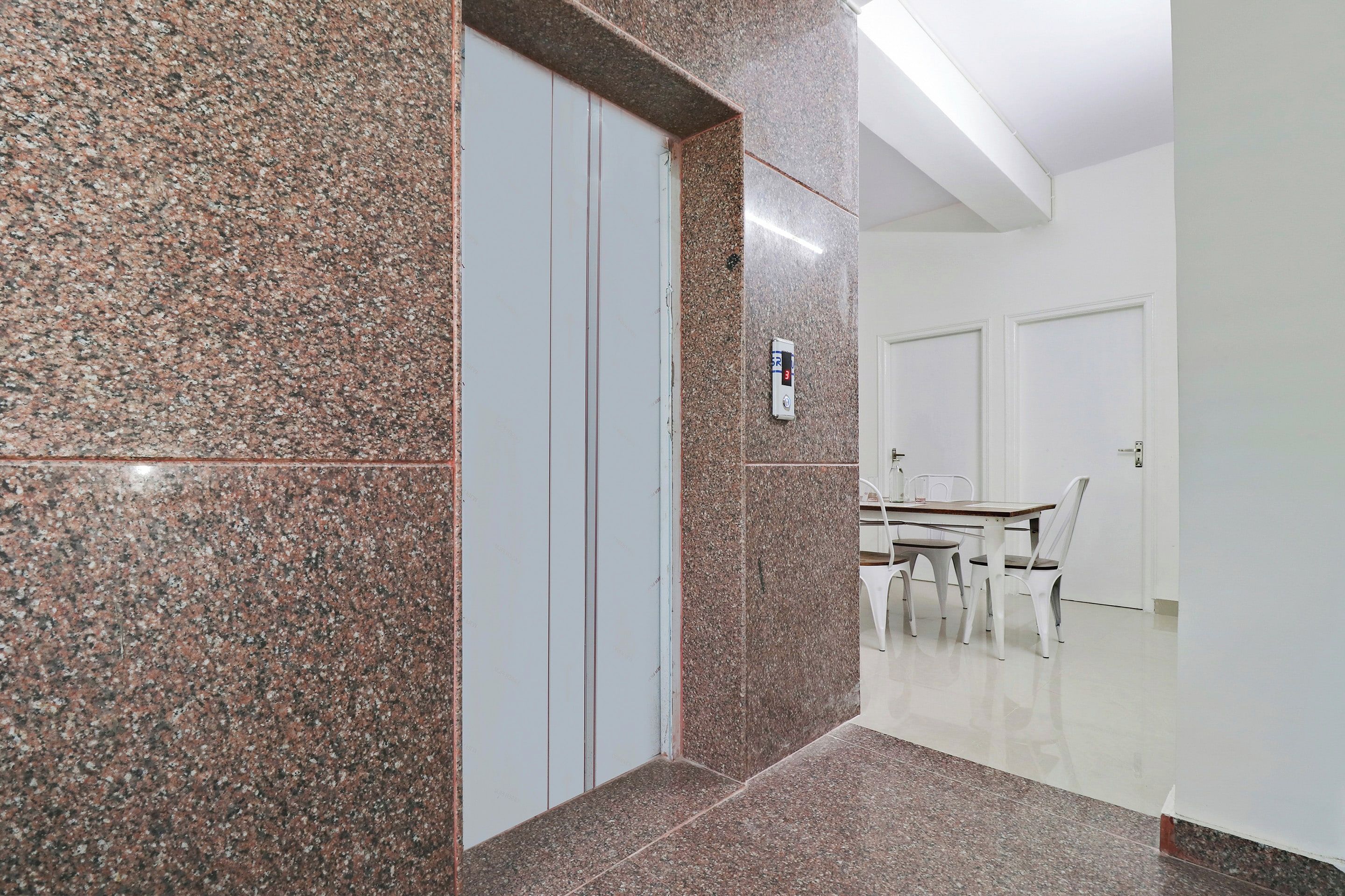 A hallway with granite walls, a white door, and a dining area with a table and chairs.
