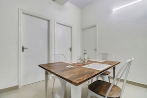 A dining area with a wooden table, white chairs, and a tiled floor. - Hotel O Leva Homes Near  (Bangalore)