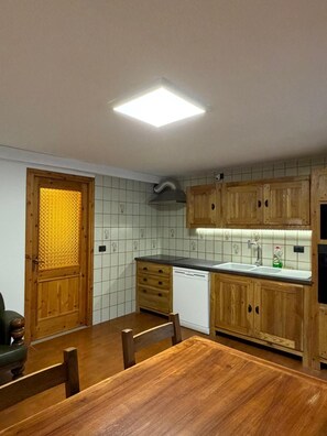A kitchen with wooden cabinets, a tiled backsplash, a built-in dishwasher, and a dining table with chairs. - Apartment 'Maison Condemines' a stone's throw from Courmayeur and La Thuile (Morgex)