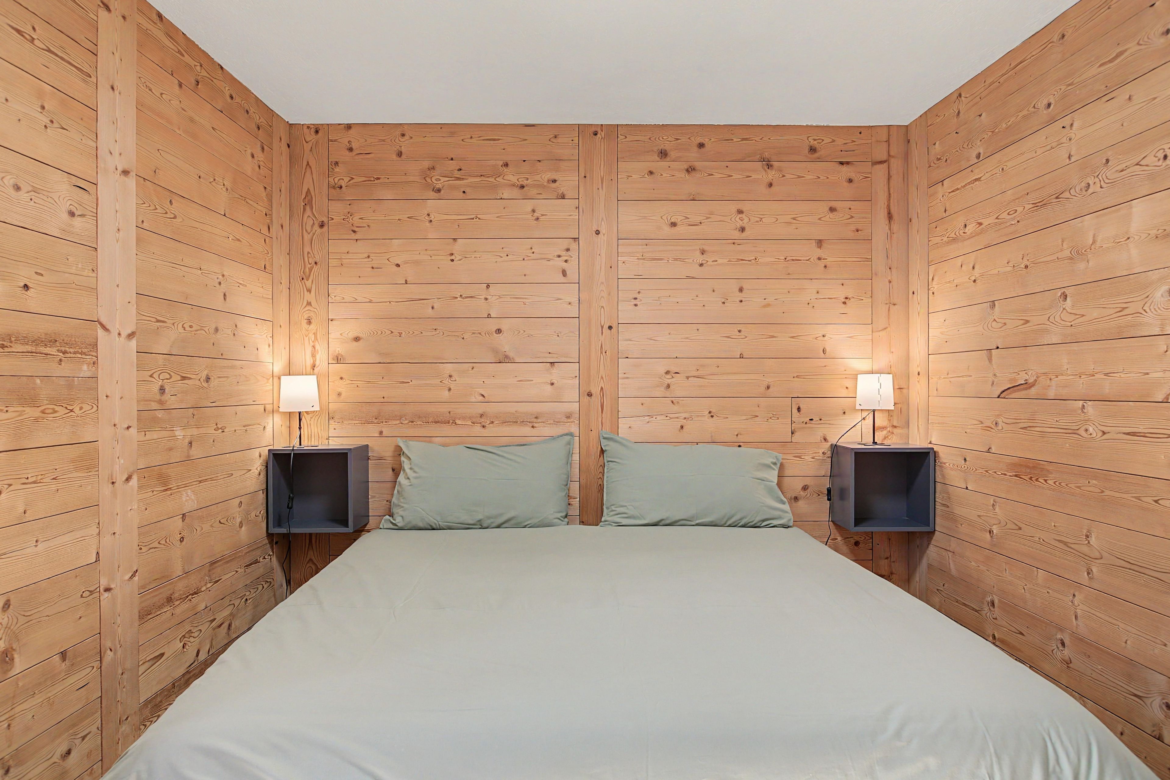 A room with a bed centered between two wooden walls, flanked by two nightstands with lamps.