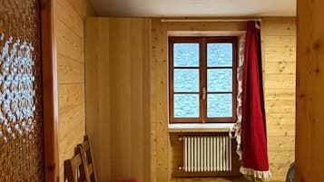 Une pièce aux murs en bois, une fenêtre donnant sur un beau paysage, un radiateur et un fauteuil rouge.