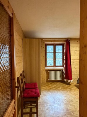A room with wooden walls, a window with a view, a radiator, and a red chair. - Apartment 'Maison Condemines' a stone's throw from Courmayeur and La Thuile (Morgex)