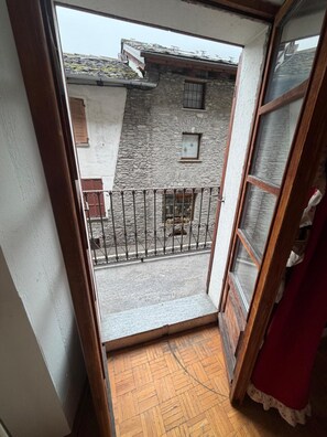 A narrow balcony with a wooden floor, a metal railing, and a view of a stone building with a window and shutters. - Apartment 'Maison Condemines' a stone's throw from Courmayeur and La Thuile (Morgex)
