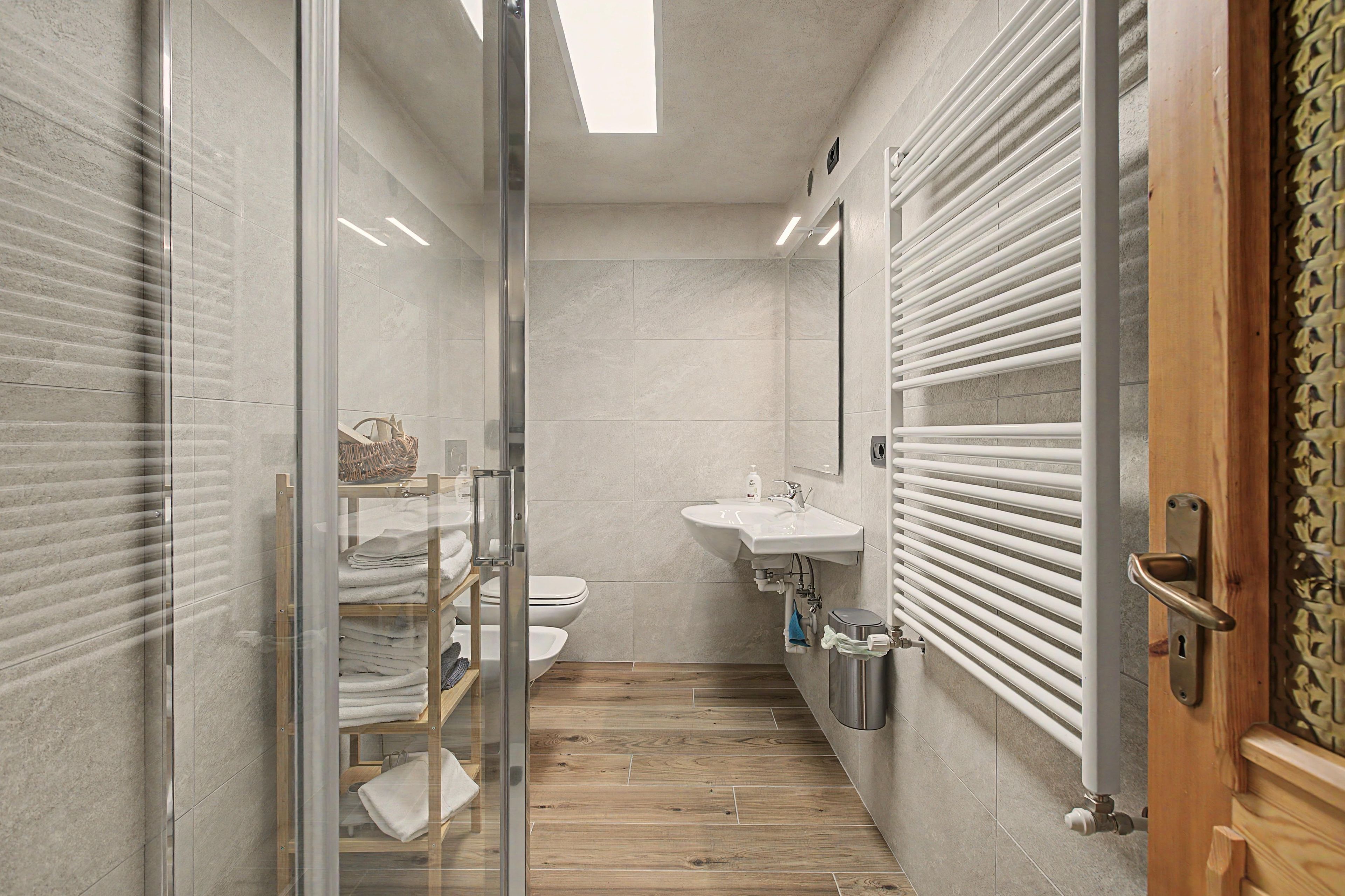 Ein modernes Badezimmer mit Duschkabine aus Glas, Holzboden, weißem Waschbecken und Handtuchhalter.