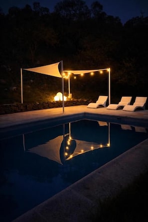 Una piscina con sillas de descanso e iluminación colgante.