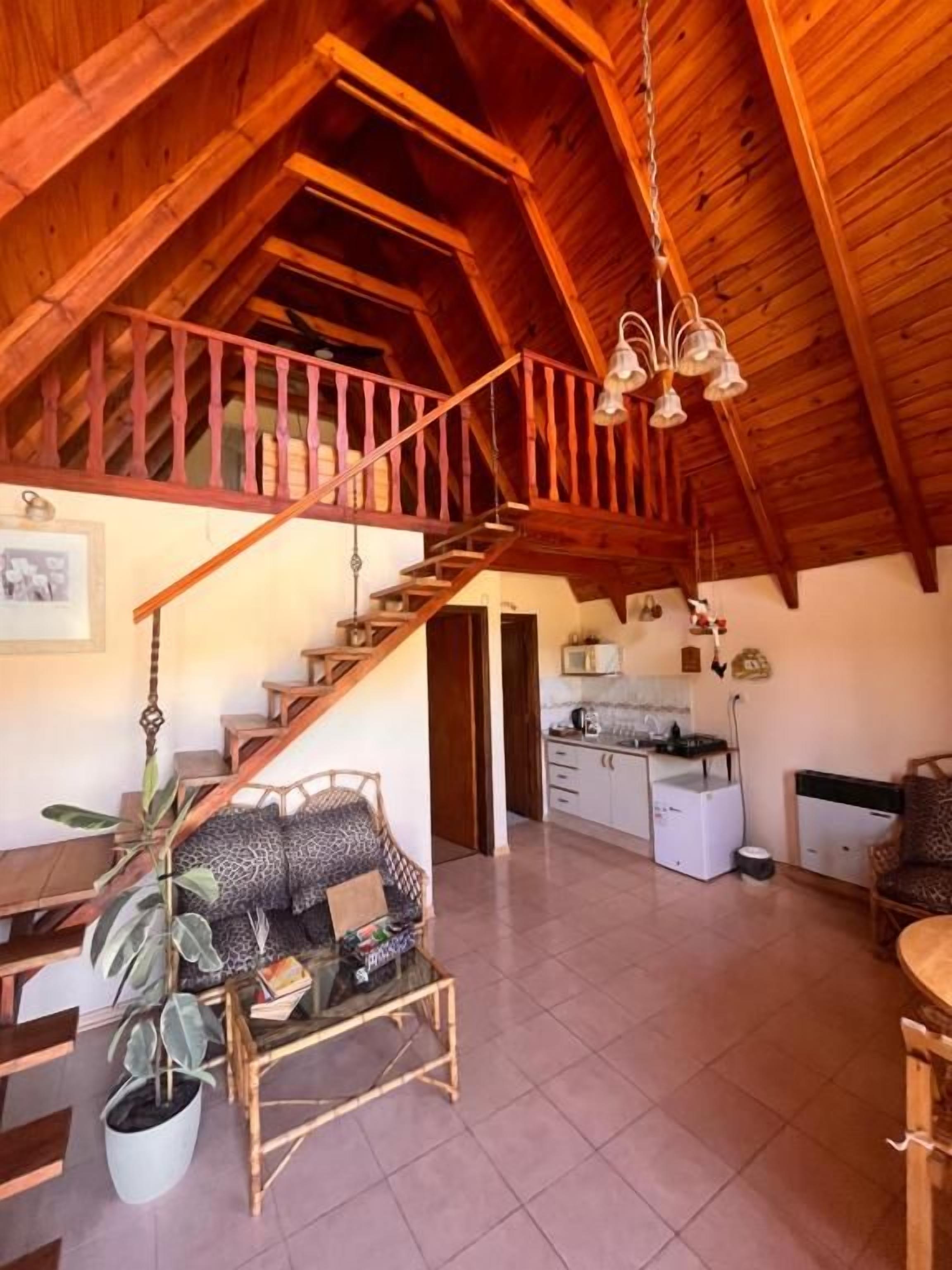 A spacious loft with a high ceiling, wooden beams, a staircase, a dining area with a table and chairs, and a kitchen area.
