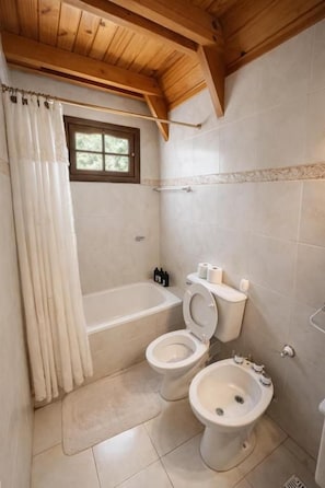 Un baño con bañera, dos inodoros, un bidé y una ventana.