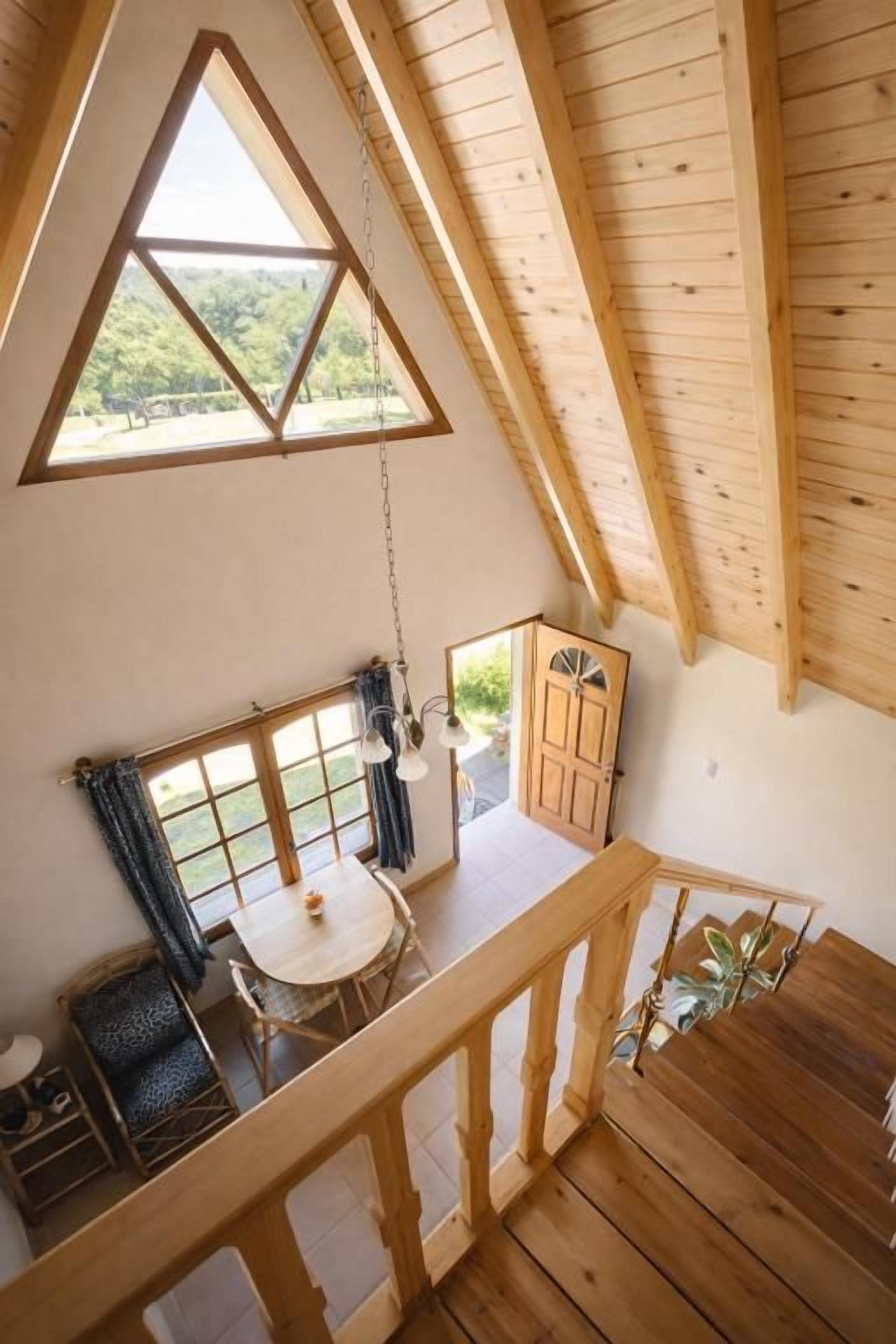 A wooden interior with a balcony, a dining table, and a view of greenery outside.