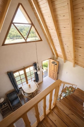 Un interior de madera con balcón, una mesa de comedor y vistas al exterior con vegetación.