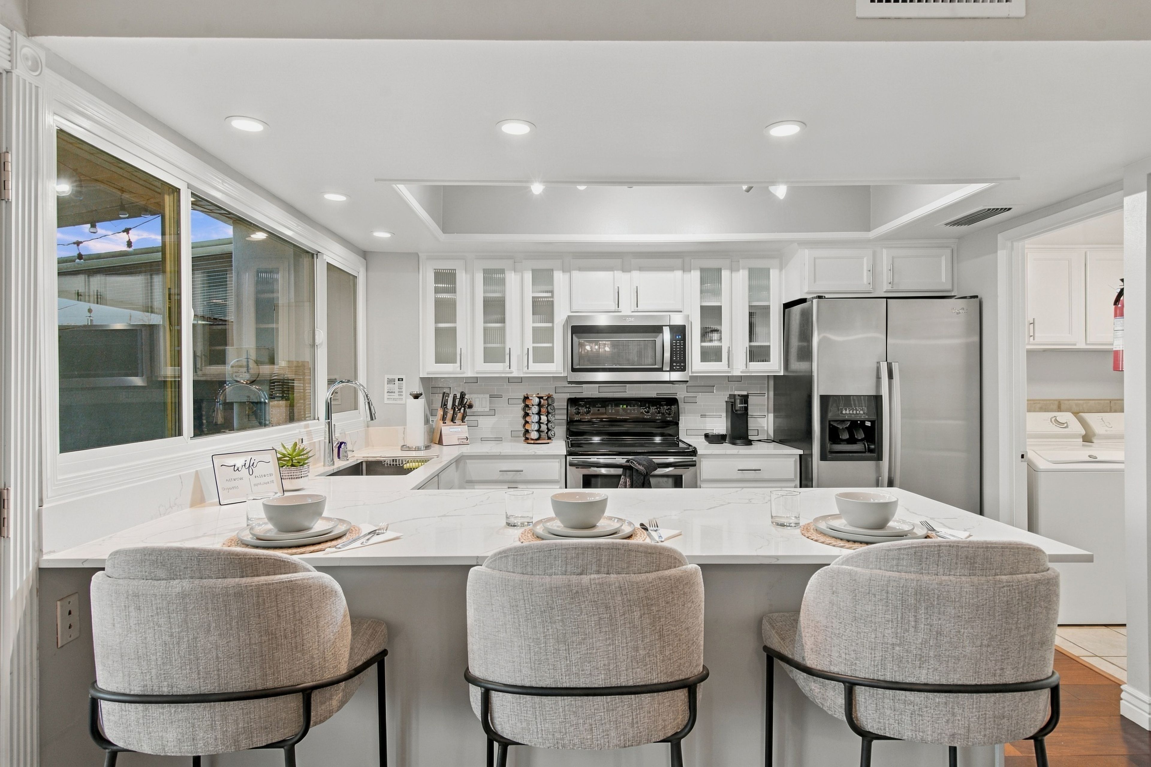 A modern kitchen with a central island, bar stools, and a large refrigerator.