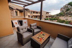 A terrace with wicker furniture, a wooden table with food and drinks, and a view of buildings and a hill. - La Roccia Vermentino Costa Paradiso, Sardinia (Costa Paradiso)