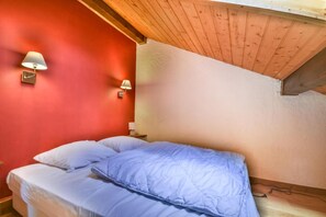 Ein Schlafzimmer mit roter Wand, Holzboden und einem Bett mit blauer Decke.