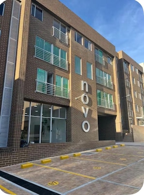 A multi-story building with the name 'Novo' on the facade, a parking area with yellow bollards, and a clear sky. - A Cozy, Stylish Stay in the Heart of Bogotá (Bogotá)