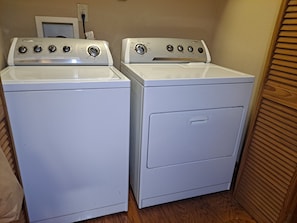 Two stacked white appliances, likely a washer and dryer, in a corner with a wooden floor and a door in the background. - A Relaxing, Rejuvenating, Rustic Retreat. (Saint Stephens Church)