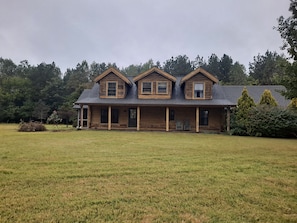 A log cabin with a porch, multiple windows, and a grassy yard. - A Relaxing, Rejuvenating, Rustic Retreat. (Saint Stephens Church)