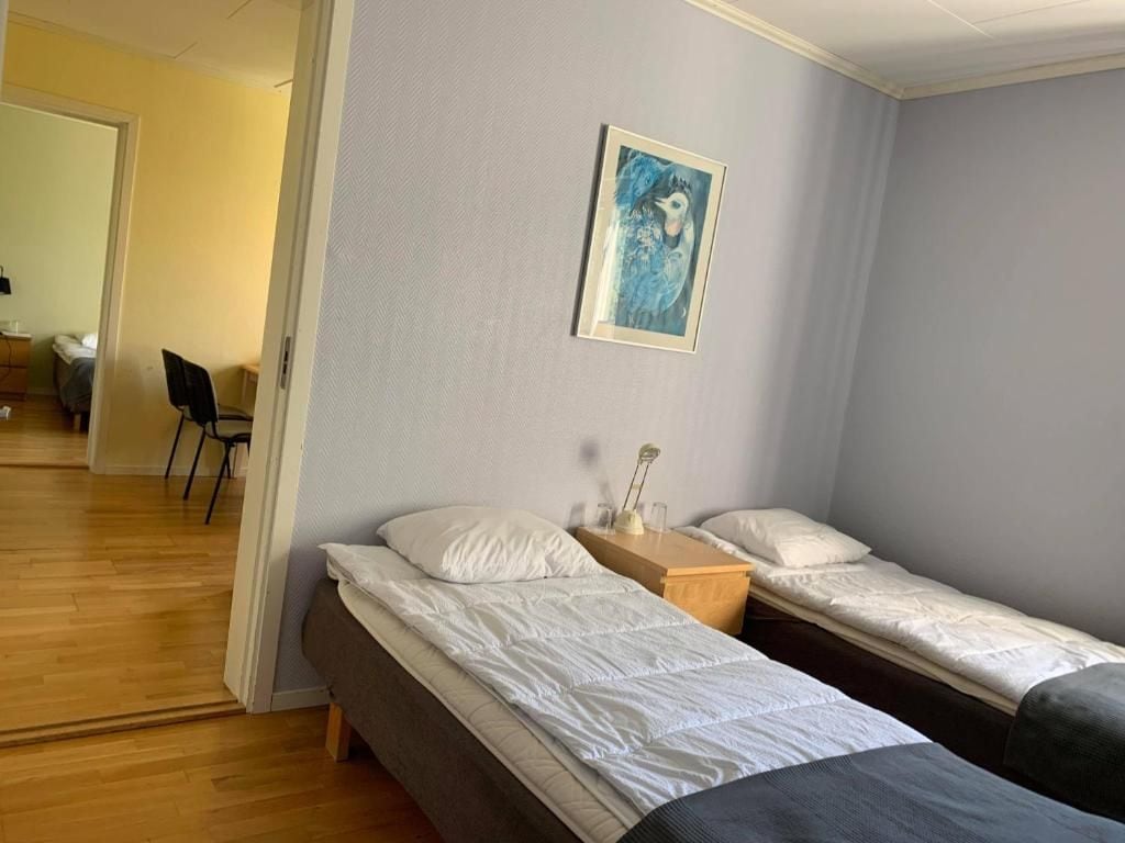 A room with two single beds, a wooden nightstand, a framed picture on the wall, and a chair in the corner.