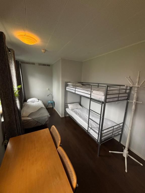 Et lille værelse med køjesenge, et træbord og en gulvlampe.