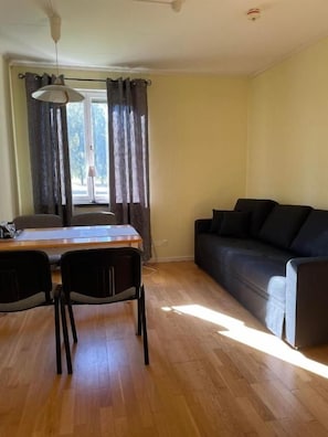 Una habitación con una mesa de comedor, dos sillas, un sofá y una ventana con cortinas.