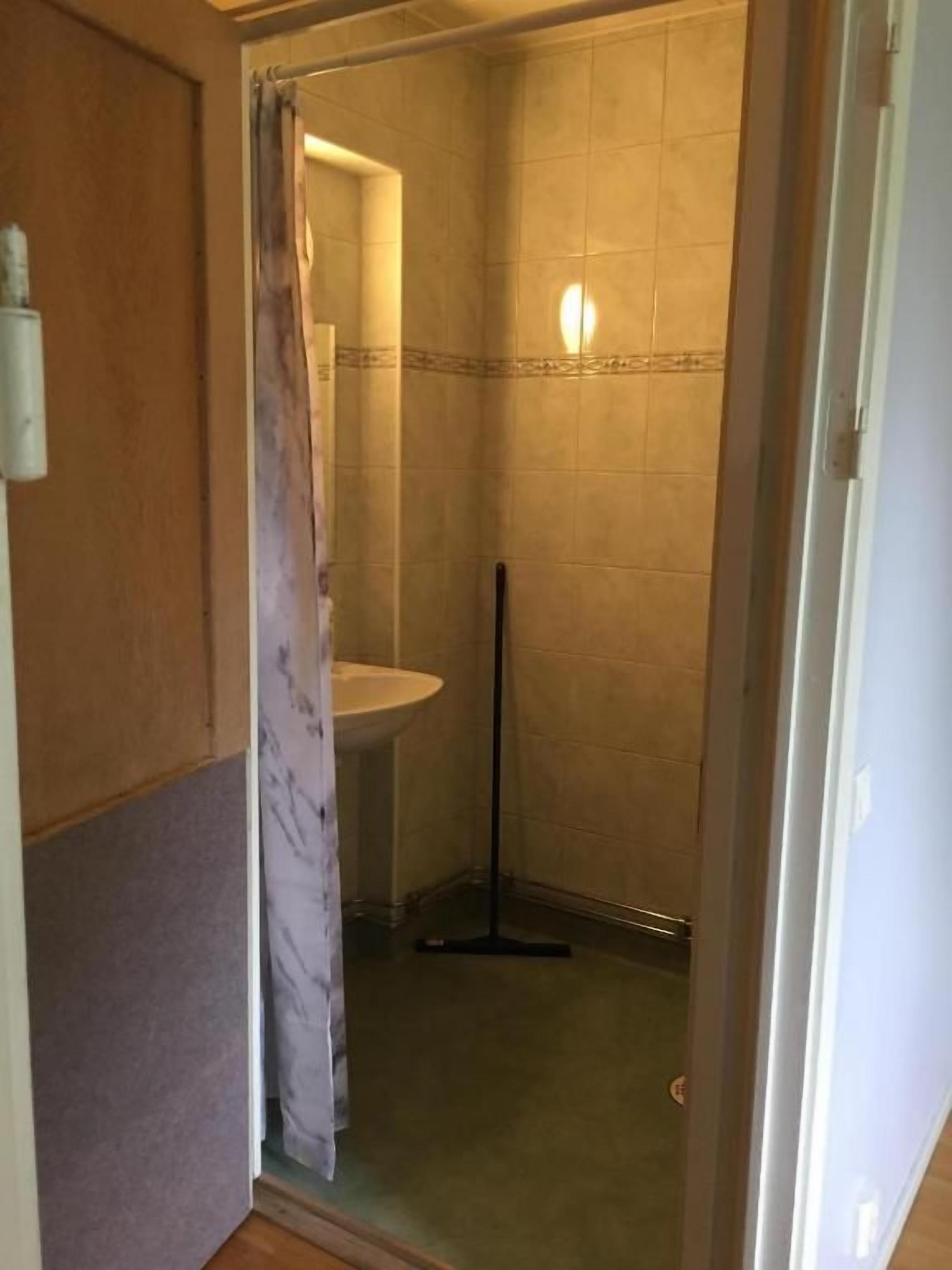 A small bathroom with a shower, a sink, and a mop.