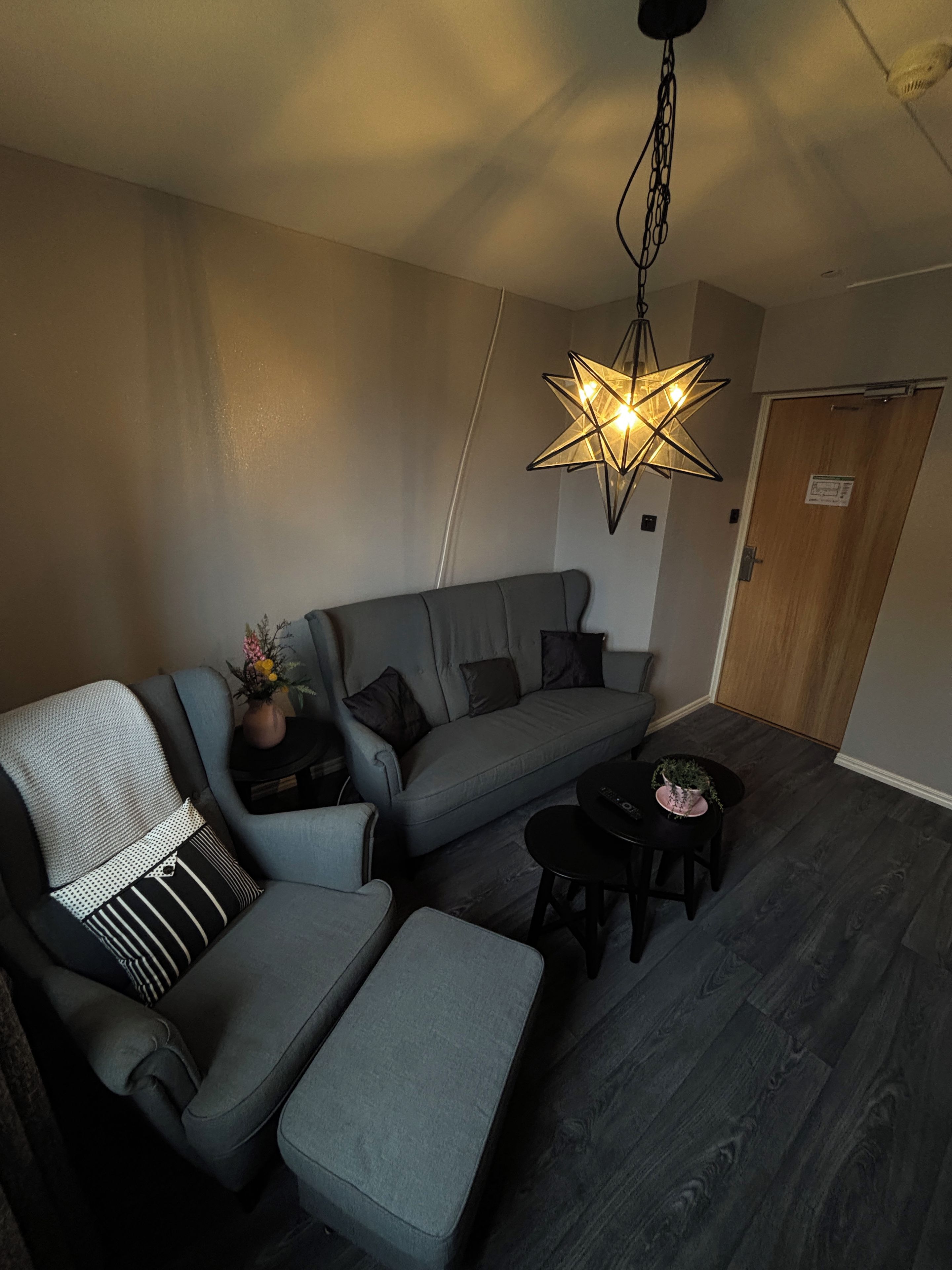 Ett modernt vardagsrum med en grå soffa, ett litet bord och en unik, stjärnformad hänglampa.