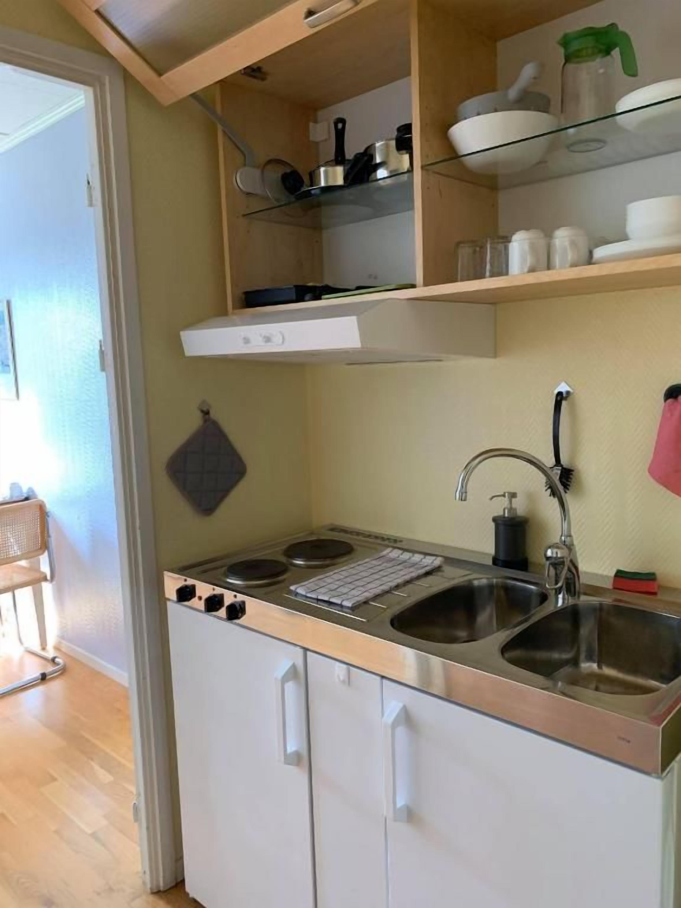 Ett kompakt kök med en inbyggd spis, ett handfat och hyllor ovanför för förvaring.