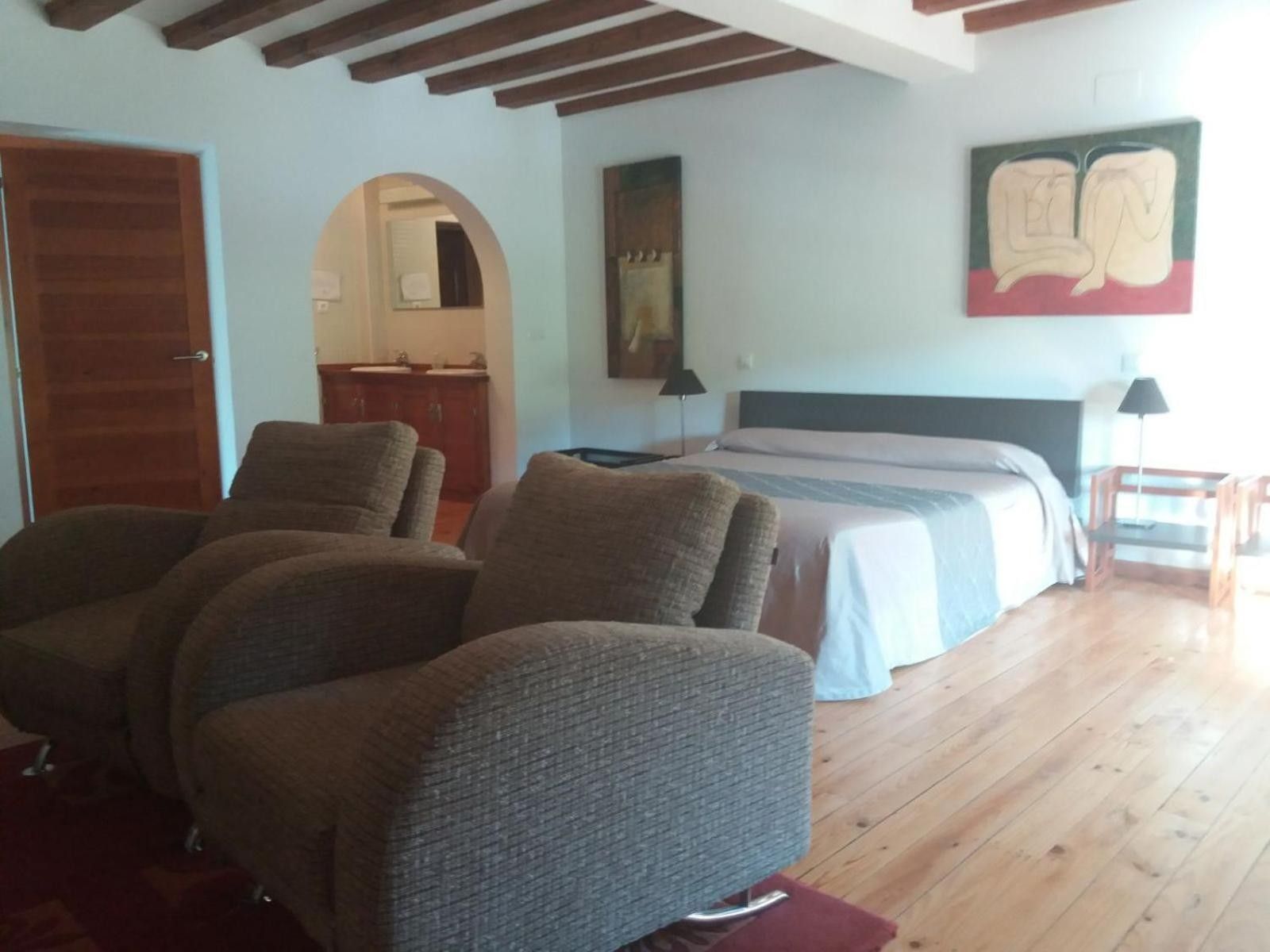 Ein Zimmer mit einem Bett, zwei Sesseln, Holzboden, einem Spiegel und einem Bild an der Wand.