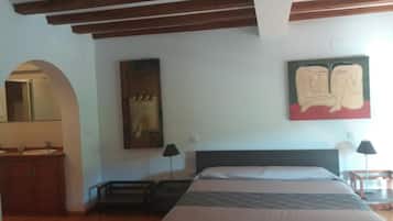 A bedroom with a wooden ceiling, a bed with a patterned bedspread, a nightstand, a mirror, and a painting on the wall.