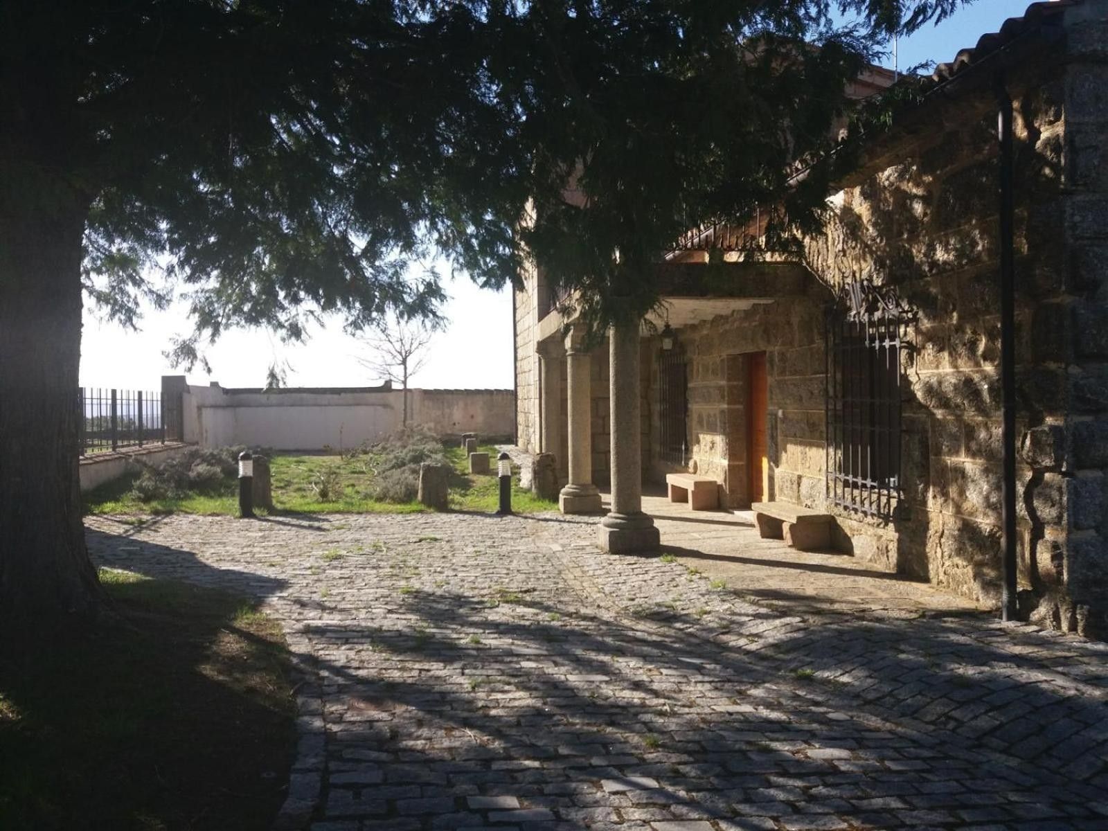 Une cour dallée de pierres, un bâtiment en pierre avec des colonnes et une clôture en arrière-plan.