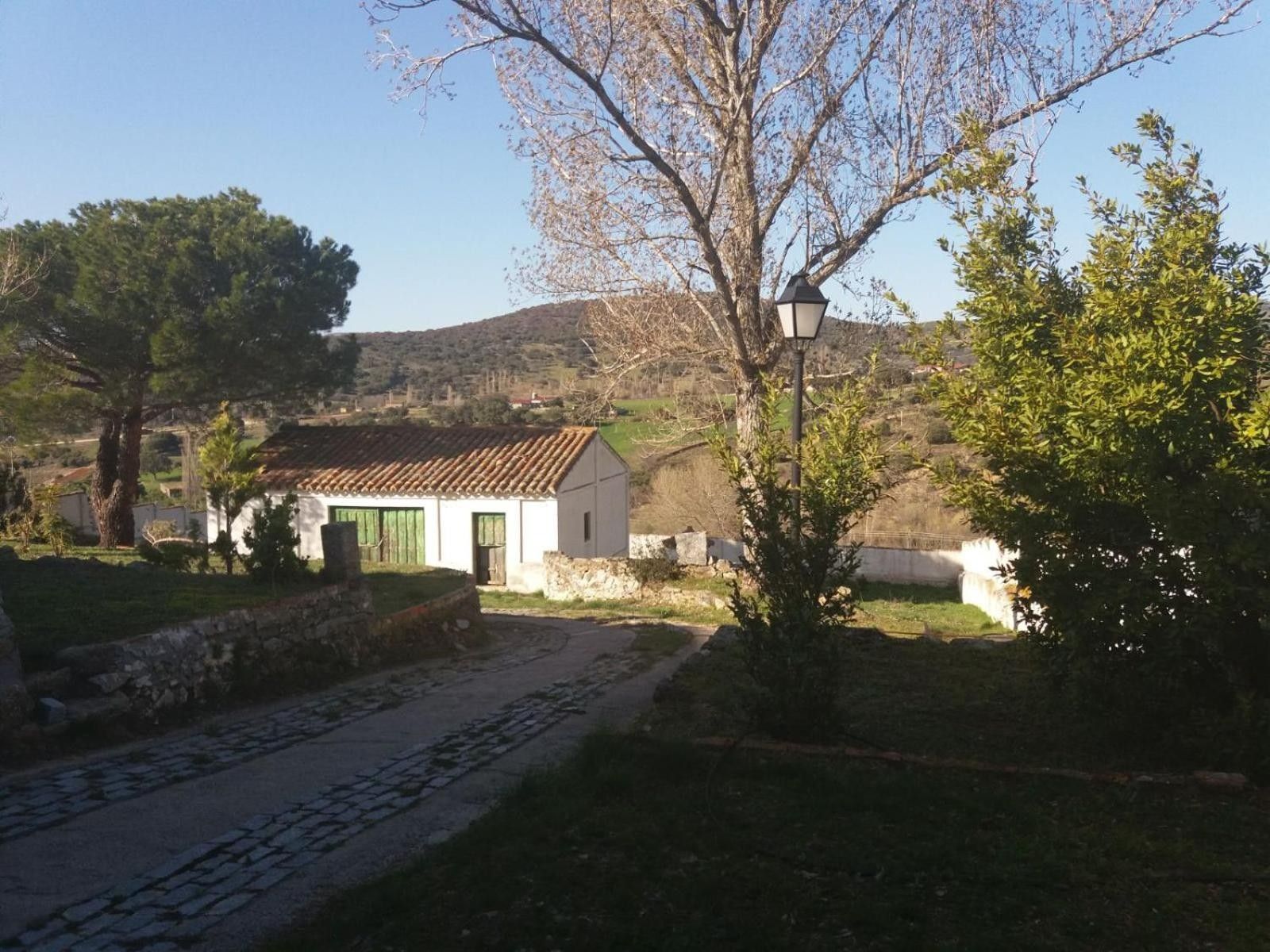 A rural setting with a white building, a cobblestone path, and a lamp post.