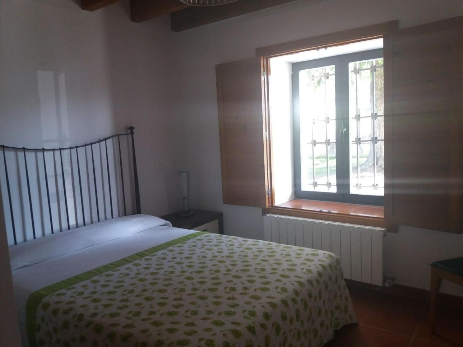 Une chambre à coucher comprenant un lit, une table de chevet, une fenêtre avec des stores et un radiateur.
