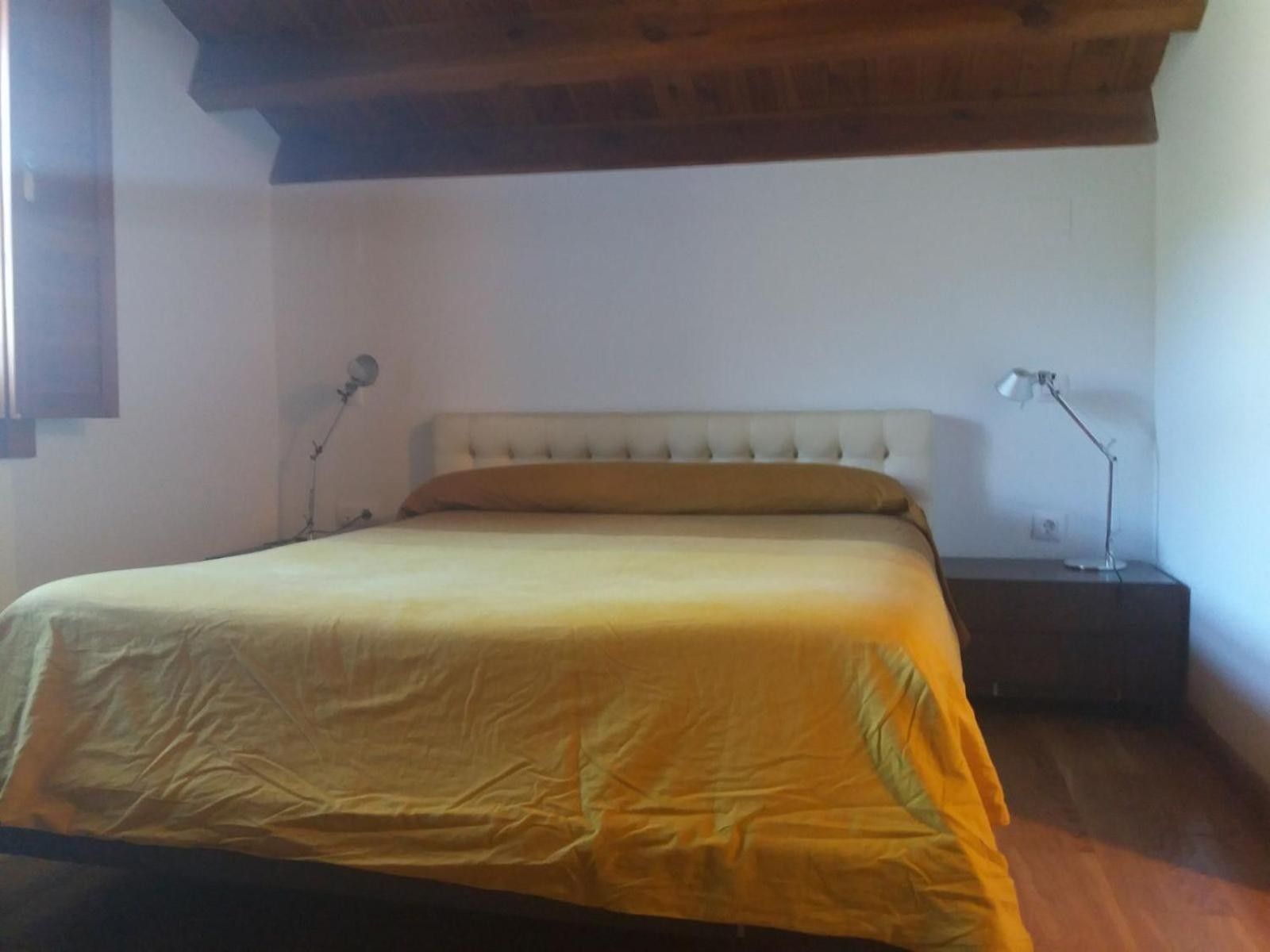 Un dormitorio con una cama, dos lámparas de noche, una mesita de noche y techo de madera.