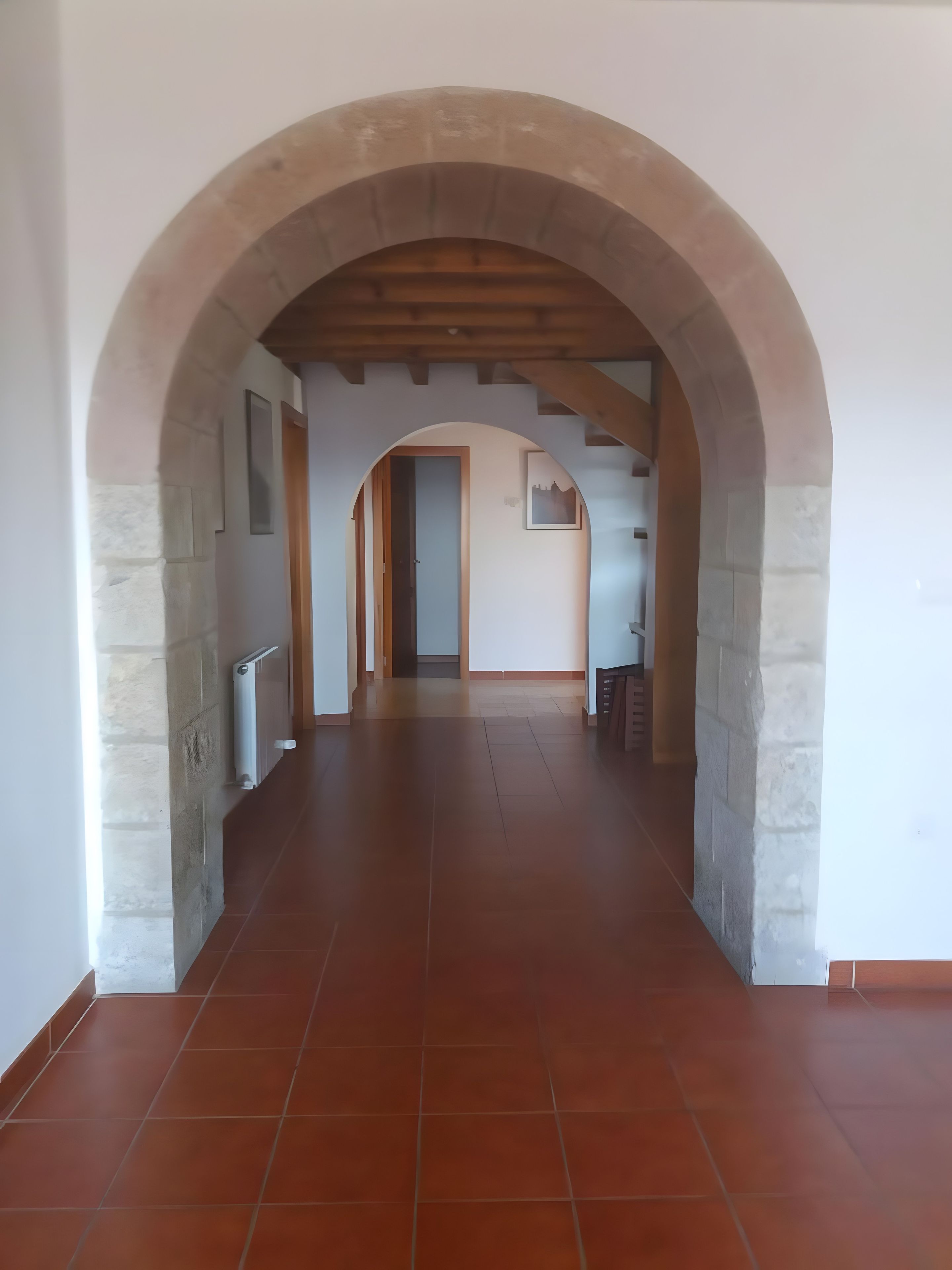 A hallway with an arched ceiling and tiled floor, leading to a door at the end.