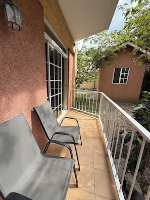 A balcony with two metal chairs, a white railing, and a view of a house and trees. - Spacious and centrally located 1 bedroom apartment in the heart of Kingston (Kingston)