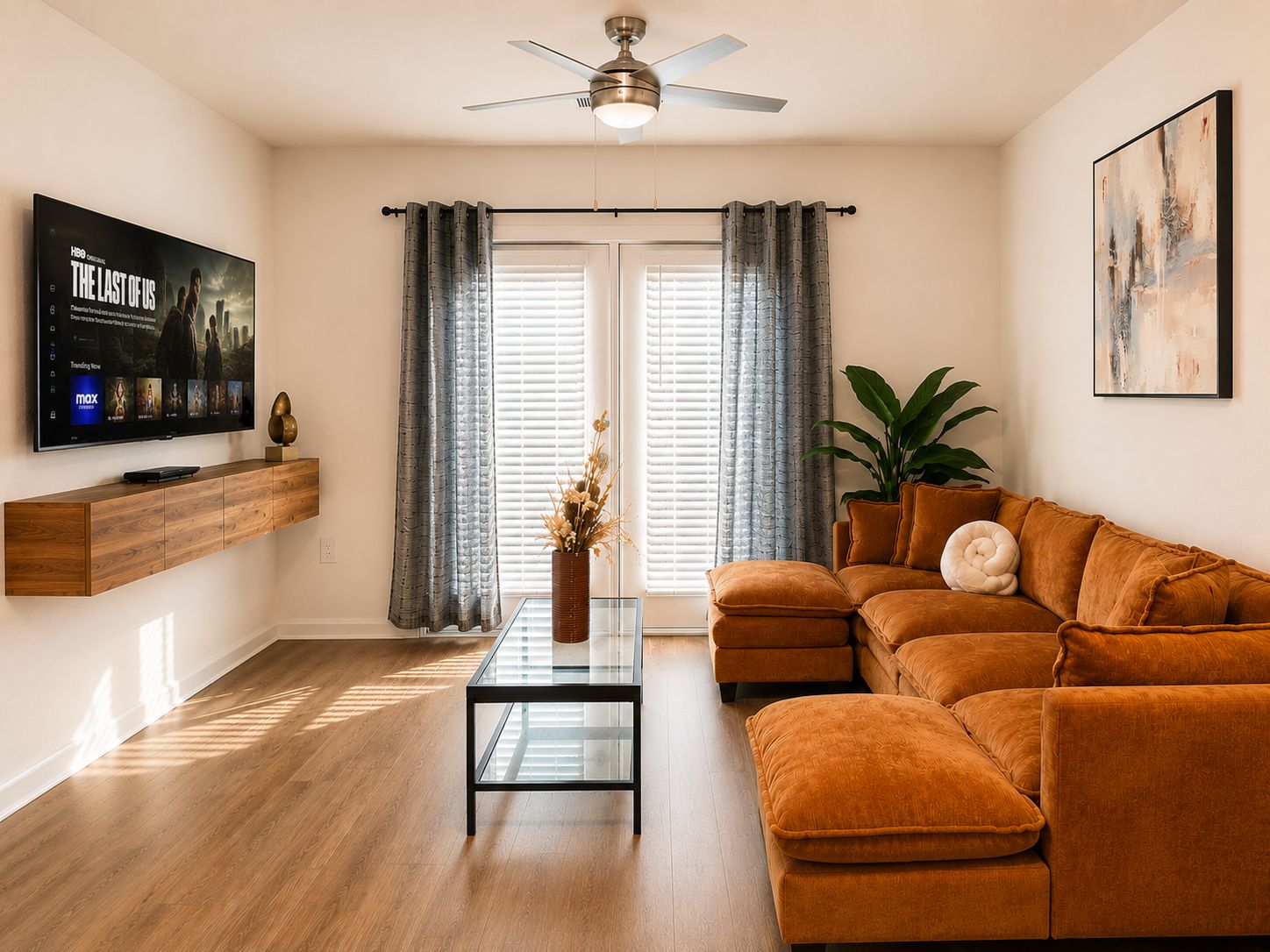 Een woonkamer met een flatscreen televisie, een plafondventilator, een bank, een salontafel en een potplant.