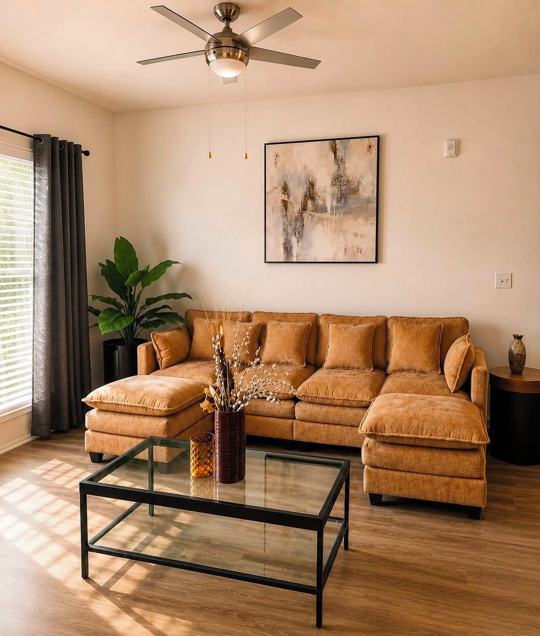 A living room with a sectional sofa, a glass coffee table, a ceiling fan, and a painting on the wall.