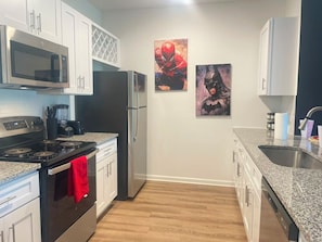 A kitchen with white cabinets, a black refrigerator, a microwave, a stove, and a sink. There are two wall-mounted paintings. - 4 min to Airport/King Bed/Pool/24hr gym/Lake view (Jacksonville)