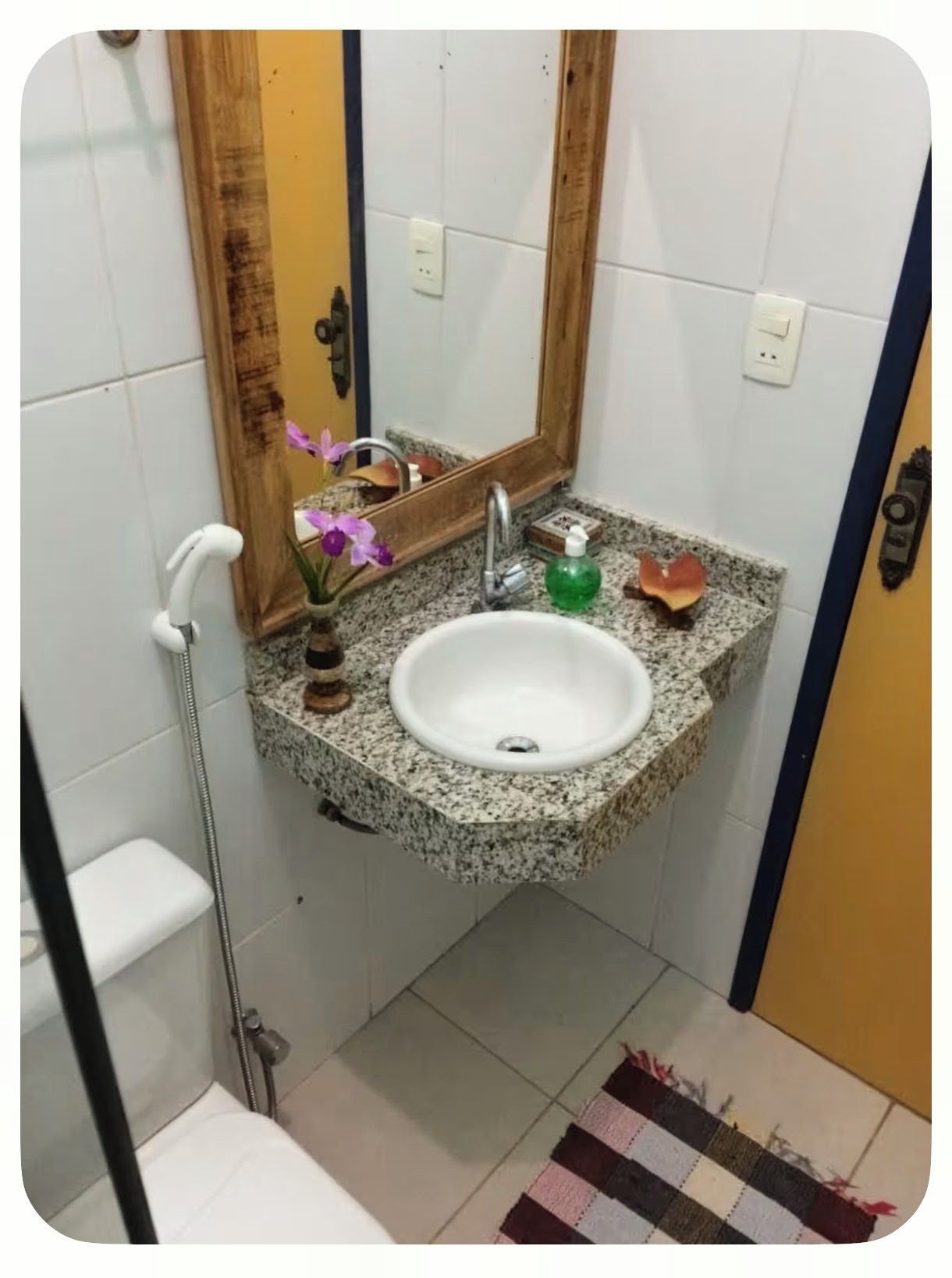Ein Badezimmer mit einem Granittisch, einem Spiegel, einer Duschbrause und einem kleinen Topfpflanzen.