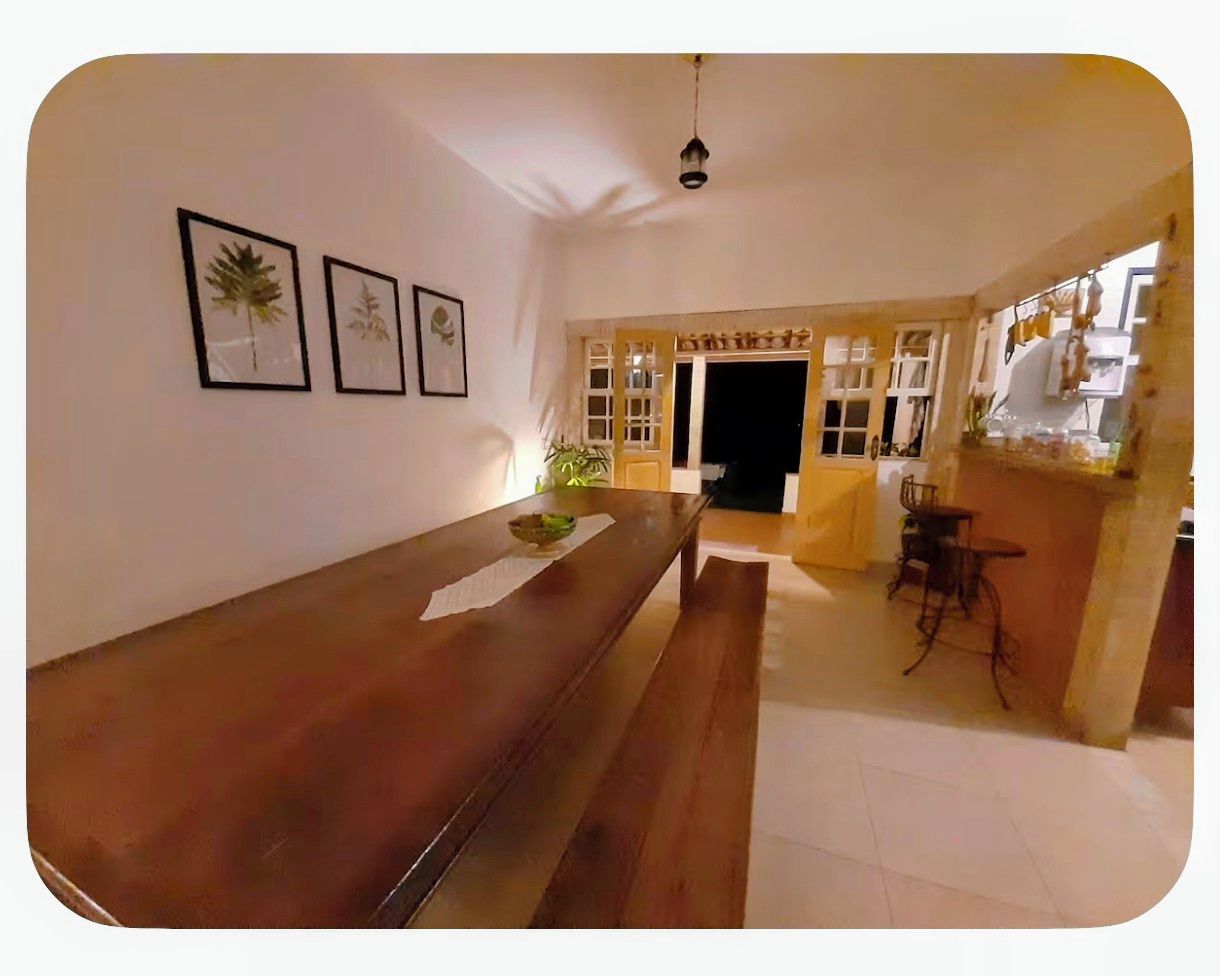 A room with a wooden bench, a dining table, and two framed botanical prints on the wall.
