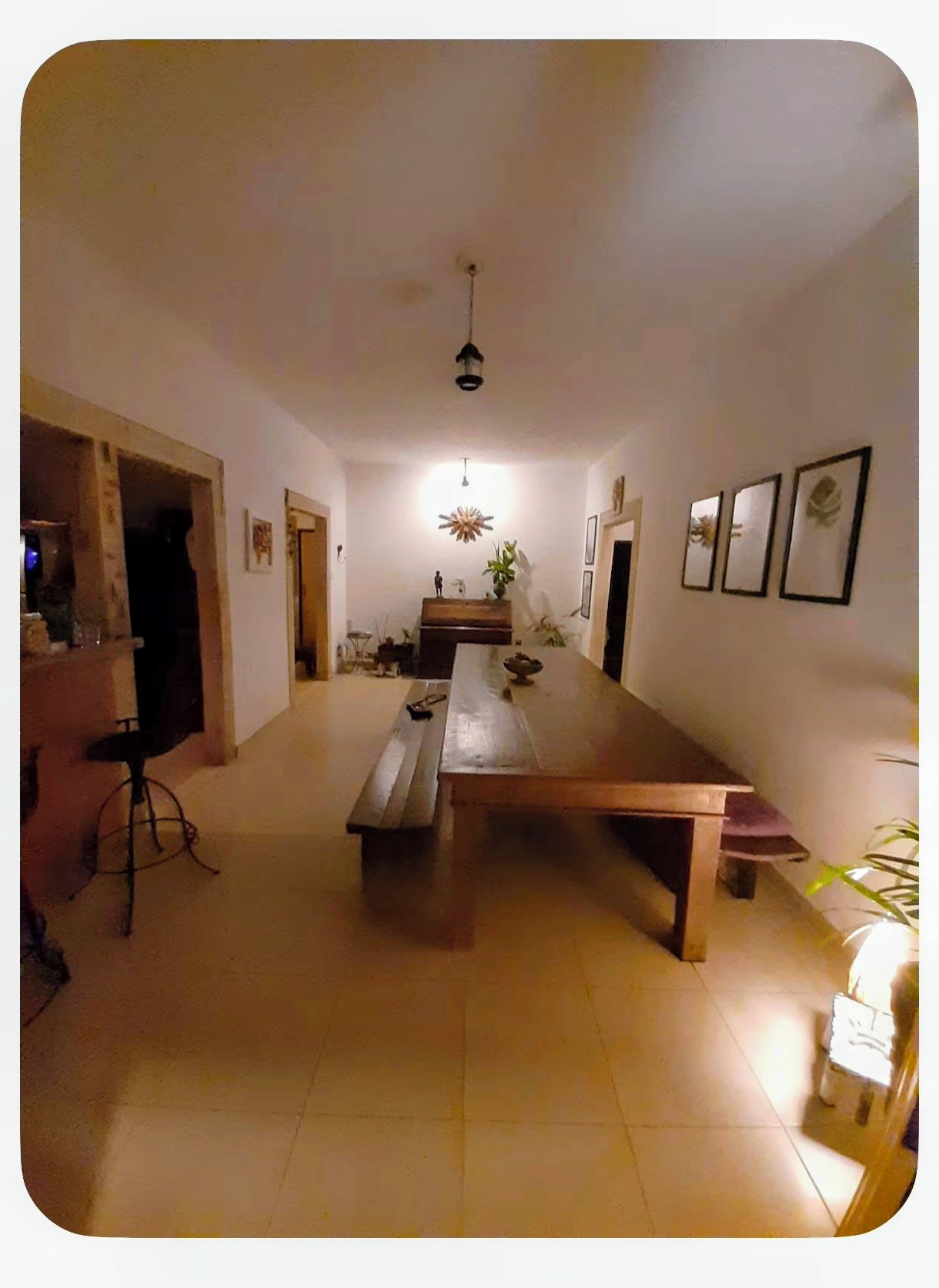 A spacious room with a long wooden table, a hanging light fixture, and framed pictures on the walls.