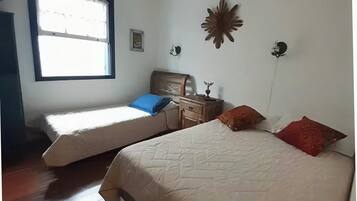 A bedroom with two beds, a nightstand, a wall clock, and a window with curtains.