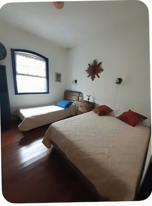 A bedroom with two beds, a nightstand, a wall clock, and a window with curtains. - Casa Bonina (Tiradentes)